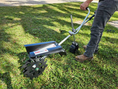 Person operating walk-behind trenching tool with extended handle cutting narrow trench in grassy lawn area