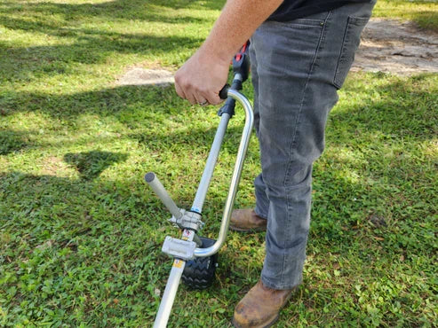 Person holding extended-handle trenching attachment with black tire on grass surface outdoors