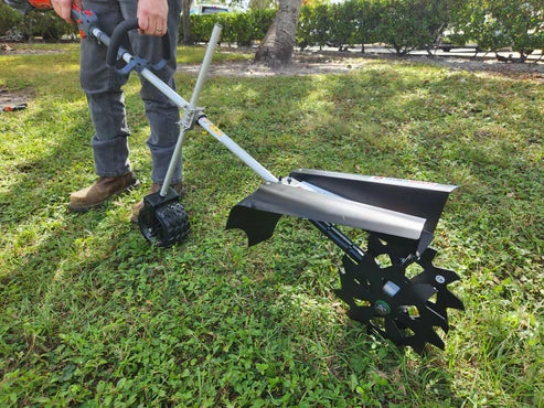 Person holding walk-behind tiller tool with star-shaped black metal wheel and angled blade on grassy surface outdoors